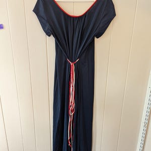 May include: A navy blue maxi dress with a red and white trim around the neckline. The dress has a tie at the waist with red and white strings.