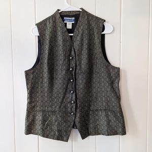 Puede incluir: Un chaleco estampado en tonos negros y dorados, abrochado y colgado de una percha blanca. El chaleco tiene un cuello alto y dos pequeños bolsillos. La marca "Pendleton" es visible en la etiqueta.