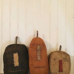 May include: Three handmade fabric pumpkins with stitched faces. The pumpkins are black, orange, and brown.