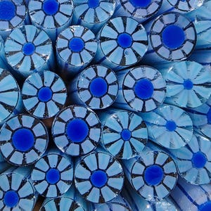 May include: A collection of cylindrical glass rods arranged in a cluster, each featuring a central deep blue circular core surrounded by a ring of alternating light blue and white petal-like segments, creating a repeating floral pattern.