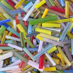 May include: A close-up shot of a pile of colorful glass rods. The rods are in various colors, including red, yellow, green, blue, and white. The rods are cylindrical and appear to be made of glass. The image is well-lit and the colors are vibrant.