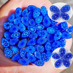 Puede incluir: Una colección de pequeñas cuentas de vidrio azul de forma ovalada con intrincados patrones azul oscuro. Las cuentas tienen varios diseños, incluyendo formas florales y geométricas. Se muestran varios grupos de cuentas en una disposición circular.