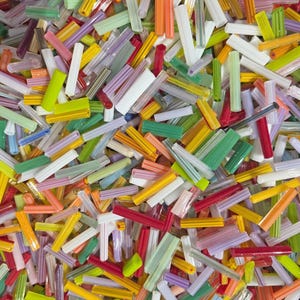 May include: A close-up shot of a vibrant assortment of colorful glass rods. The rods are in various shades of red, yellow, green, orange, white, and purple. The rods are scattered, creating a textured and visually appealing pattern.