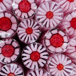 May include: Close-up of flower-shaped hard candies. Each candy has a red center and white petals, wrapped in clear cellophane. The candies are arranged closely together, creating a colorful and textured pattern.