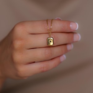 May include: A gold chain necklace with a small rectangular pendant featuring a black star in the centre.