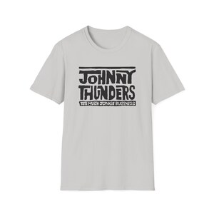 Puede incluir: Camiseta gris claro con la inscripción "JOHNNY THUNDERS" en negro, con una fuente audaz y desgastada. Debajo, la frase "TOO MUCH JUNKIE BUSINESS". La camiseta tiene mangas cortas y cuello redondo.