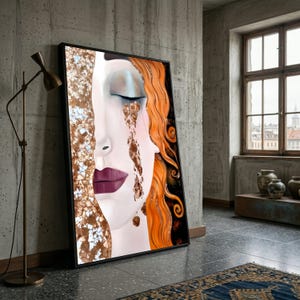 Op de afbeelding: Een ingelijste kunstdruk met een gestileerd portret van een gezicht met gesloten ogen en vloeiend oranje haar. Het kunstwerk heeft een surrealistische kwaliteit, waarbij één kant van het gezicht lijkt te bestaan uit getextureerde, goudkleurige elementen en de andere kant een lichte huidskleur heeft.