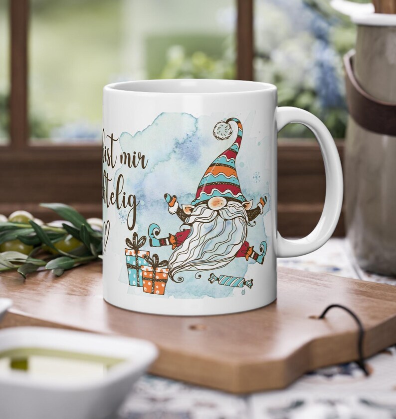 Puede incluir: Taza de cer&aacute;mica blanca con un dise&ntilde;o de gnomo caprichoso con una larga barba blanca, un sombrero colorido y regalos. La taza tiene el texto "Du bist mir wichtig" en una fuente de escritura, sobre un fondo azul acuarela.