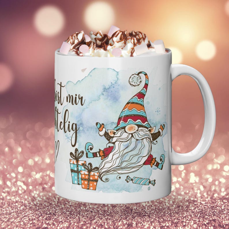 Puede incluir: Taza de cer&aacute;mica blanca con un dise&ntilde;o de gnomo caprichoso, una larga barba blanca, un sombrero colorido y cajas de regalo. La taza est&aacute; llena de crema batida, malvaviscos y salsa de chocolate. La taza tiene el texto "ist mir heilig".