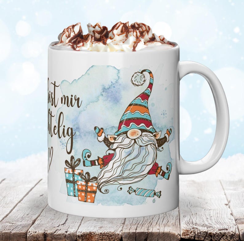 Puede incluir: Taza de cer&aacute;mica blanca con una ilustraci&oacute;n caprichosa de gnomo, texto y cobertura de crema batida con salsa de chocolate. El gnomo lleva un sombrero colorido y sostiene regalos. La taza est&aacute; sobre una superficie de madera.