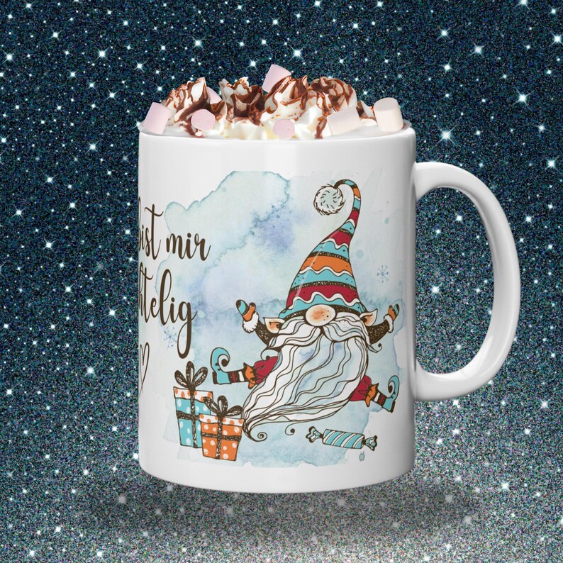 Puede incluir: Taza de cer&aacute;mica blanca con una ilustraci&oacute;n caprichosa de un gnomo, cubierta con crema batida, salsa de chocolate y malvaviscos. El gnomo lleva un sombrero colorido y tiene una larga barba blanca. La taza tiene el texto "ist mir selig" y est&aacute; decorada con regalos y caramelos.