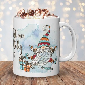 Puede incluir: Taza de cer&aacute;mica blanca con un dise&ntilde;o de gnomo caprichoso con una larga barba blanca y un sombrero colorido. La taza tiene el texto "... bist mir..." y est&aacute; llena de crema batida y virutas de chocolate. Tambi&eacute;n se presentan regalos y caramelos.