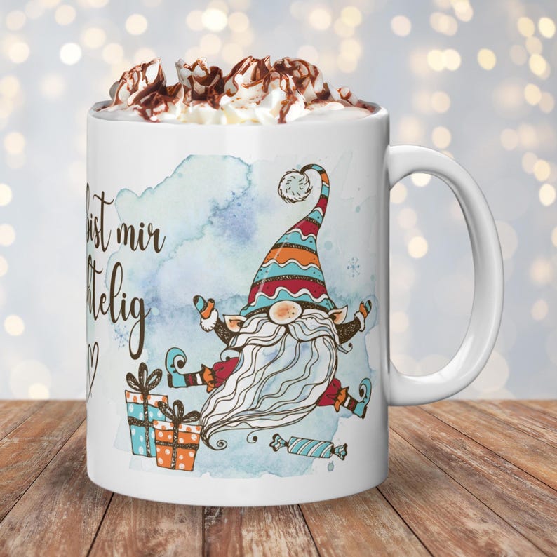 Puede incluir: Taza de cer&aacute;mica blanca con un dise&ntilde;o de gnomo caprichoso con una larga barba blanca y un sombrero colorido. La taza tiene el texto "... bist mir..." y est&aacute; llena de crema batida y virutas de chocolate. Tambi&eacute;n se presentan regalos y caramelos.