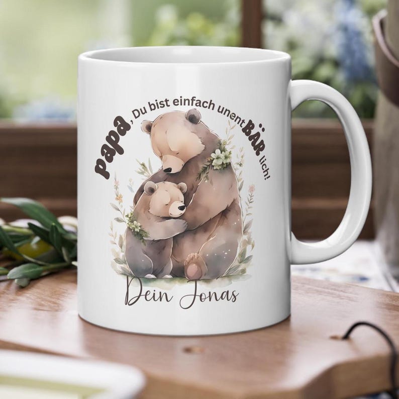Op de afbeelding: Witte keramische mok met een aquarel illustratie van twee beren die elkaar omhelzen. De mok heeft Duitse tekst: "papa, Du bist einfach unentB&Auml;Rlich! Dein Jonas."