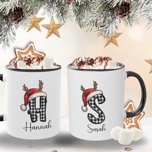 Personalisierte Weihnachtstasse mit einer stilvollen Initiale im karierten Design, die von einer niedlichen Rentier-Weihnachtsmütze geziert wird. Mit Wunschname erhältlich – ideal für ein einzigartiges und persönliches Geschenk.