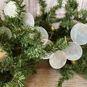 May include: Close-up of a Christmas tree branch decorated with round, translucent, white ornaments. The ornaments are attached to the green branches. Small, warm-toned lights are interspersed throughout the branches.