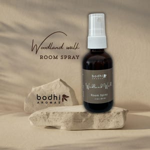 May include: A brown glass bottle with a white spray nozzle filled with room spray. The label reads "bodhi aromas Woodland Walk Room Spray 1 oz | 30 ml".