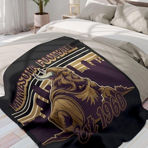 Puede incluir: Manta de tiro negra con un diseño vintage que presenta a un guerrero vikingo sosteniendo un escudo y una espada. El texto "Minnesota Football Est. 1960" está impreso en la manta.