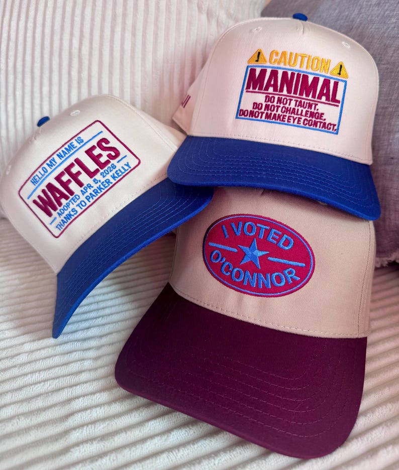 Puede incluir: Tres gorras de b&eacute;isbol con dise&ntilde;os &uacute;nicos. Una gorra tiene el texto "HELLO MY NAME IS WAFFLES" con una visera azul. Otra gorra tiene el texto "CAUTION MANIMAL" con una visera azul. La tercera gorra tiene el texto "I VOTED O'CONNOR" con una visera burdeos.