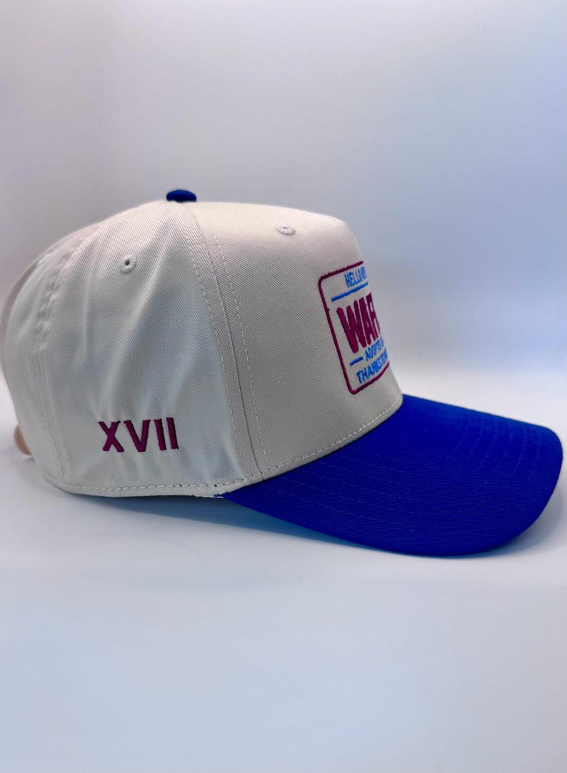 Puede incluir: Gorra de b&eacute;isbol con corona crema y visera azul. La gorra presenta un parche rectangular con la palabra "WAR" en texto rojo y azul. El n&uacute;mero romano "XVII" est&aacute; bordado en el lateral.
