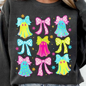 May include: Dark gray sweatshirt featuring a colorful graphic of ghost-like figures with bows. The design includes yellow, pink, and blue ghosts with star accents and checkered bows. The sweatshirt has a crew neck.