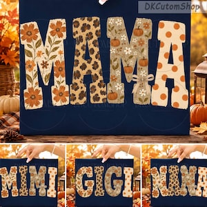 Op de afbeelding: Een donkerblauw t-shirt met het woord MAMA in grote blokletters. Elke letter heeft een uniek patroon, waaronder oranje bloemen, luipaardprint, pompoenen met witte bloemen en oranje stippen op een crèmekleurige achtergrond.