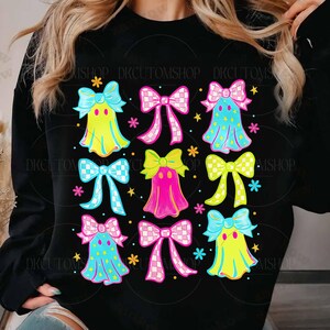 May include: Black sweatshirt featuring a colorful pattern of ghost-like figures with bows. The ghosts are in shades of yellow, pink, and blue, with star and flower accents. The bows have checkered and striped patterns.