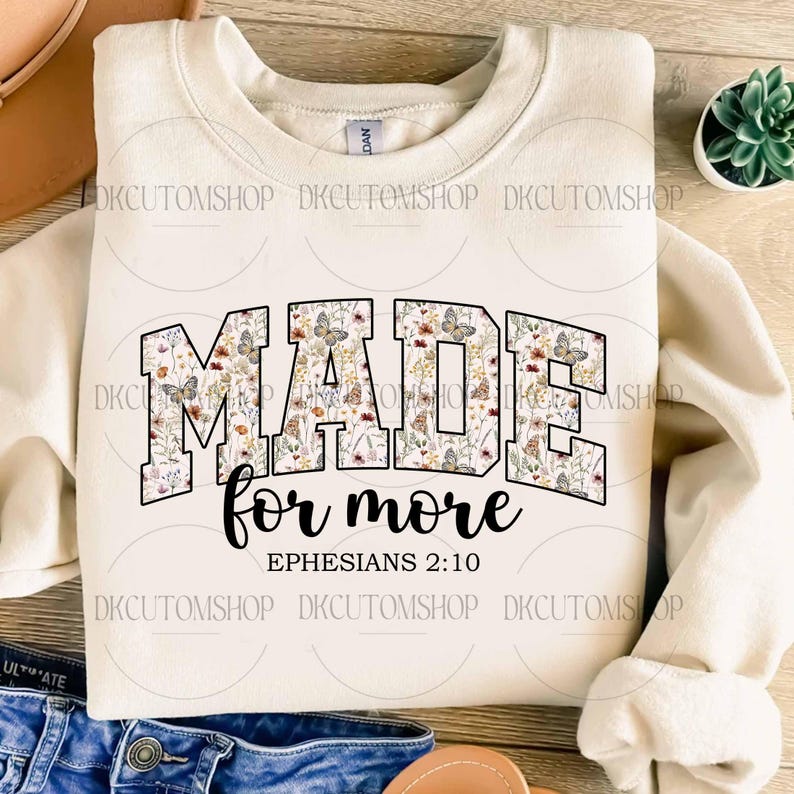 Puede incluir: Sudadera color crema con las palabras "MADE for more" en un dise&ntilde;o floral con mariposas. El texto "Efesios 2:10" est&aacute; debajo. La sudadera es de estilo casual y c&oacute;modo.