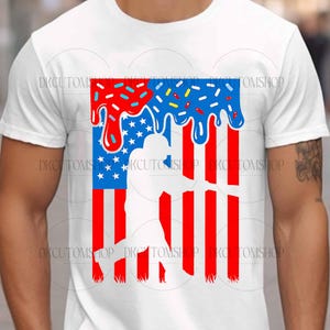 May include: White t-shirt featuring a patriotic design. The graphic combines elements of the American flag with a baseball player silhouette. The top portion has a dripping effect with red, white, and blue sprinkles.