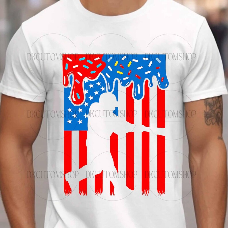 May include: White t-shirt featuring a patriotic design. The graphic combines elements of the American flag with a baseball player silhouette. The top portion has a dripping effect with red, white, and blue sprinkles.