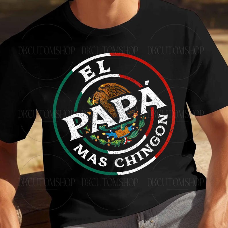 Puede incluir: Camiseta negra con un dise&ntilde;o circular. El texto "EL PAP&Aacute; MAS CHINGON" est&aacute; en blanco, verde y rojo. El dise&ntilde;o incluye un emblema de &aacute;guila marr&oacute;n y un borde verde y blanco, que representa la bandera mexicana.