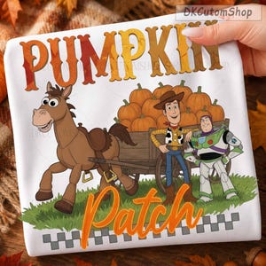 May include: A white t-shirt featuring a graphic of a brown horse pulling a wooden wagon filled with orange pumpkins. Beside the wagon stand two cartoon characters, one in a cowboy outfit and one in a space suit. The text PUMPKIN Patch is printed.
