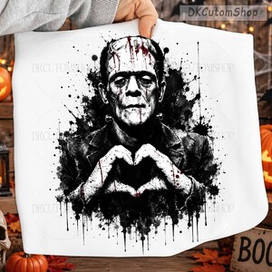 May include: A white fabric item featuring a black and white watercolor-style illustration of Frankenstein's monster making a heart shape with hands. The design includes red blood-like splatters and the text DKCutomShop in the top right corner.