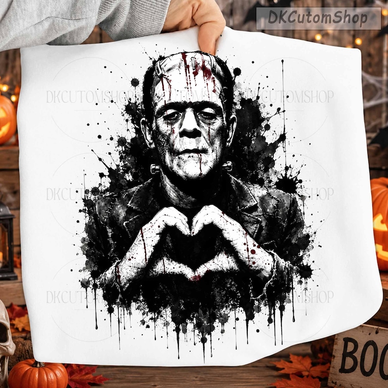 May include: A white fabric item featuring a black and white watercolor-style illustration of Frankenstein's monster making a heart shape with hands. The design includes red blood-like splatters and the text DKCutomShop in the top right corner.