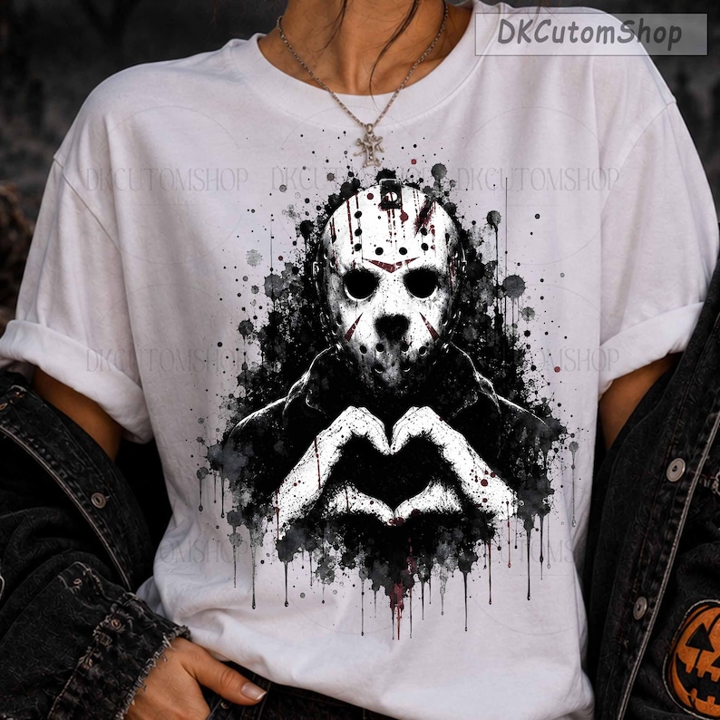 May include: A white short-sleeve t-shirt featuring a graphic print of a hockey mask-wearing character in black and white with red accents. The character is making a heart shape with their hands against a black ink splatter background.