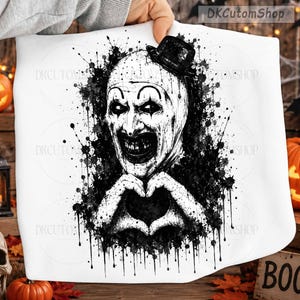 May include: A white fabric item featuring a black ink-style graphic of a clown wearing a small top hat. The clown has a white face with dark eye makeup and a wide, dark, toothy grin. The hands are positioned to form a heart shape below the chin.