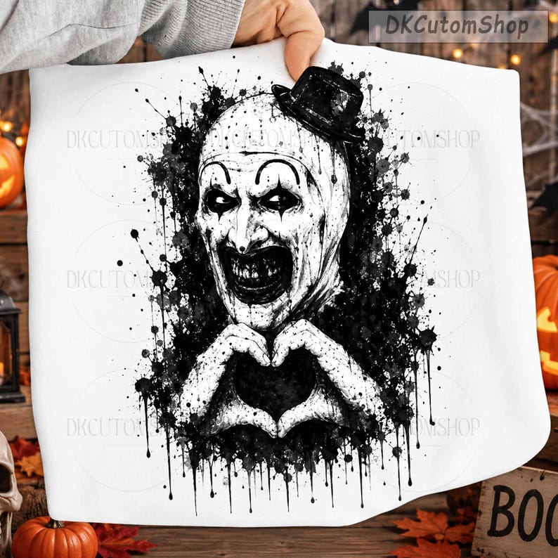May include: A white fabric item featuring a black ink-style graphic of a clown wearing a small top hat. The clown has a white face with dark eye makeup and a wide, dark, toothy grin. The hands are positioned to form a heart shape below the chin.