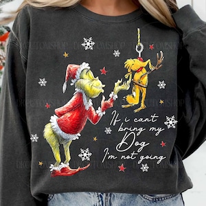 Puede incluir: Sudadera gris oscuro con un personaje de Grinch con traje de Papá Noel y un perro amarillo con cuernos. El texto dice "If I can't bring my Dog I'm not going." Copos de nieve blancos y estrellas rojas dispersas.