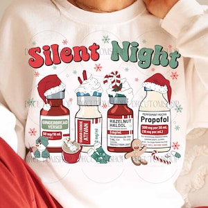 Op de afbeelding: Witte sweatshirt met de woorden "Silent Night" in rood en groen. Het ontwerp toont vier flessen met kerstthema labels, waaronder "Gingerbread Versed" en "Peppermint Mocha Propofol". Feestelijke sneeuwvlokken en vakantiegraphics maken het ontwerp compleet.