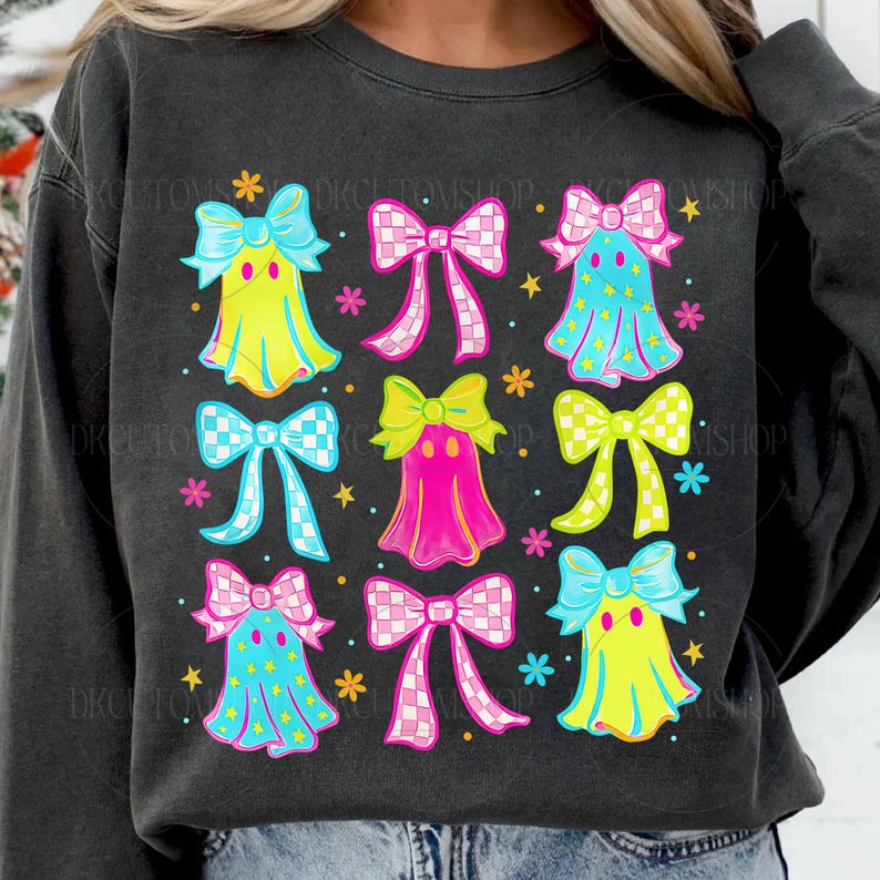 May include: Dark gray sweatshirt featuring a colorful graphic of ghost-like figures with bows. The design includes yellow, pink, and blue ghosts with star accents and checkered bows. The sweatshirt has a crew neck.