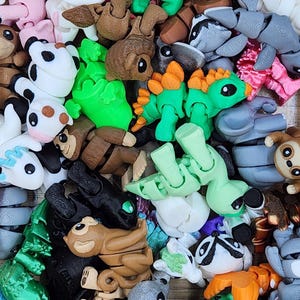 Puede incluir: Una colección de pequeñas figuras de animales articuladas impresas en 3D en plástico, de varios colores y especies, incluyendo dinosaurios, monos y criaturas míticas. Cada figura cuenta con articulaciones segmentadas para movimiento.