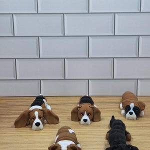 May include: Five different dog breeds made of brown, black and white clay. The dogs are lying down on a wooden surface.