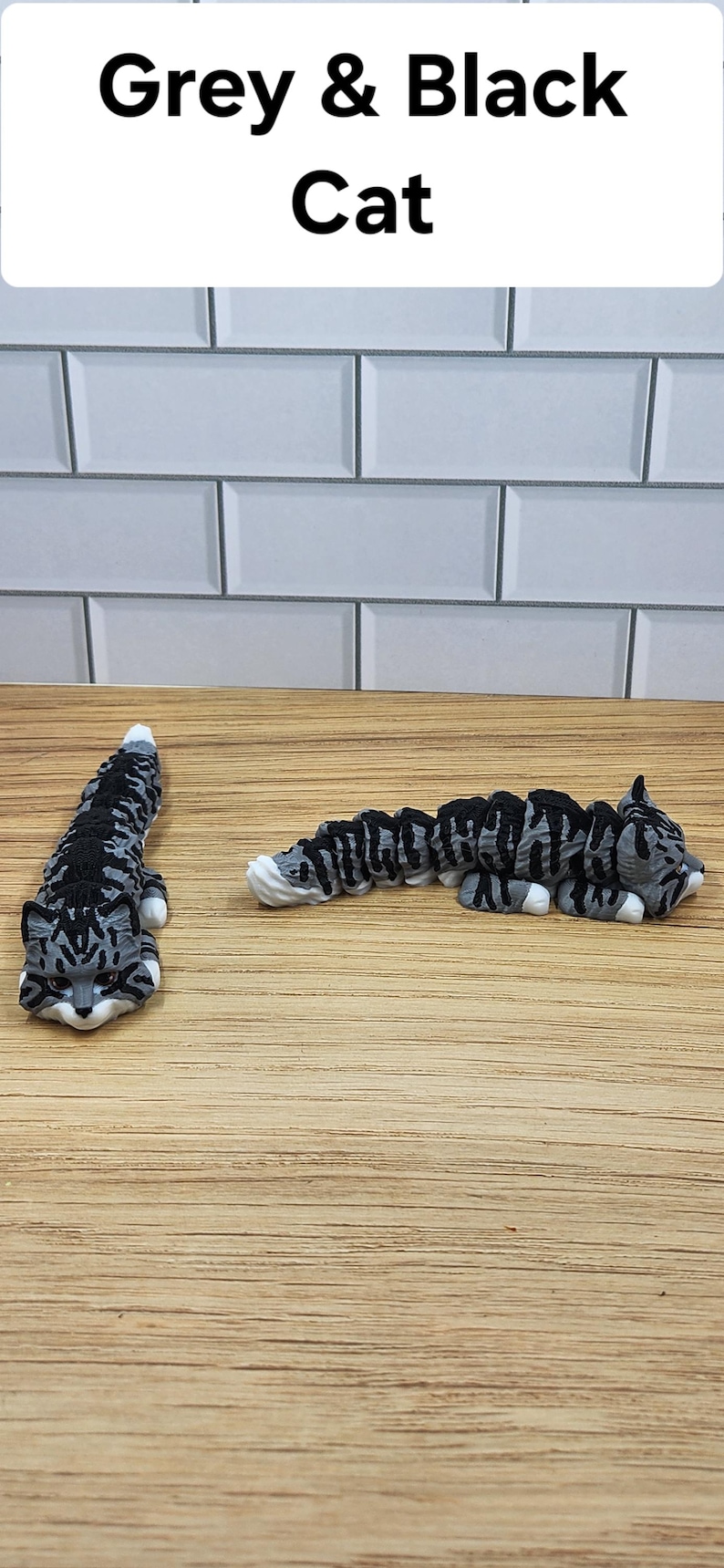 May include: Two gray and black tabby cats, one lying down and one curled up, on a wood surface. The text "Grey & Black Cat" is above the cats.