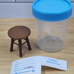 Puede incluir: Un recipiente de pl&aacute;stico transparente para muestras con una tapa azul, un peque&ntilde;o taburete marr&oacute;n y una etiqueta que dice "STERILE Ready for Use" y "STOOL". La etiqueta tambi&eacute;n incluye campos para la informaci&oacute;n del paciente y un s&iacute;mbolo de riesgo biol&oacute;gico.