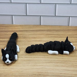 May include: Two black and white cat figurines lying on a wooden surface. The cats are curled up in a sleeping position.