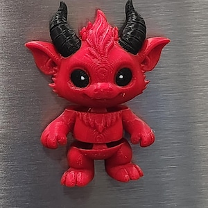May include: A small, red, three-dimensional printed creature figurine featuring two black curved horns, large black eyes with white highlights, pointed ears, and a textured surface. The figure has a segmented body design with a visible gap at the waist.