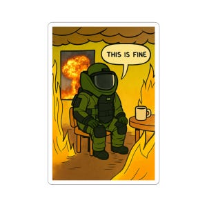 Op de afbeelding: Een sticker met een cartoon illustratie van een persoon in een bompak die rustig in een brandende kamer zit. Een tekstballon zegt "THIS IS FINE". Een mok staat op een kleine tafel. De achtergrond toont vlammen en een explosie.