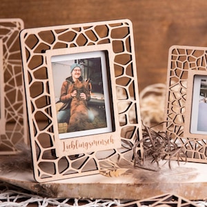 Könnte beinhalten: Holz-Fotorahmen mit einem geometrischen Muster. Die Rahmen halten kleine Fotos und werden auf einer Holzoberfläche ausgestellt. Ein Rahmen trägt das Wort "Lieblingsmensch".