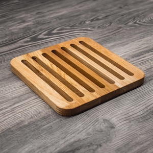 Op de afbeelding: Een vierkante houten broodplank met parallelle groeven. De plank is gemaakt van lichtgekleurd hout met een natuurlijke afwerking. De groeven lopen over het oppervlak en creëren een textuur. Ontworpen voor het serveren of snijden van brood.