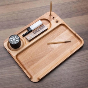Op de afbeelding: Een houten rolling tray met een aansteker, grinder en een pakje Gizeh vloeitjes. De tray heeft een ingebouwde houder voor een vloeitje en een kleine houten deuvel. De tray is gemaakt van lichtgekleurd hout.